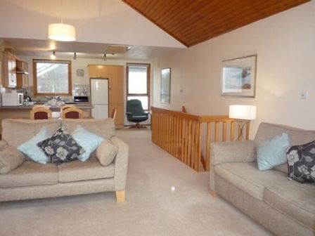 A living room with sofas and cushions and a kitchen area with a refrigerator and dining chairs at 16 Keswick Bridge in Keswick