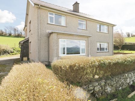 The exterior of a two-story house with hedges and a stone wall at Tai Candryll in Llanrwst