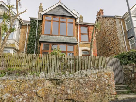 A front view of a two-story stone house with wooden framed windows a wooden fence and stone wall at Chy-an-Brae in Newquay