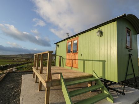 A green wooden shepherd hut with steps and a small deck on a concrete base at Cysgod y Bugail in Holyhead