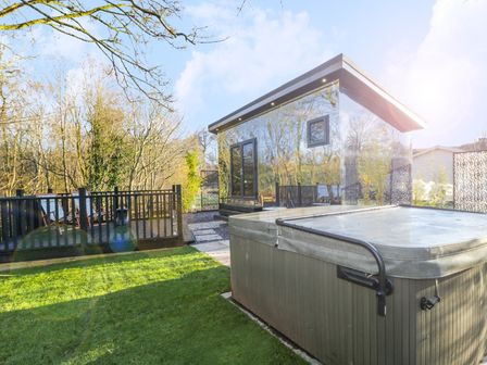 A garden with a hot tub and a mirrored cabin near a deck with chairs at Reflection in Longtown