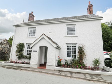 A white two-story house with a small porch and plants along the front at Llys Alaw in Llangernyw