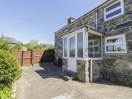 A stone exterior of a house with a white enclosed porch and a wooden gate in a fenced yard at Ty Uchaf in Dyffryn Ardudwy