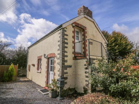 A small stone cottage with a white door and a small balcony on the upper floor at Bwthyn Y Jacdo in Crymych