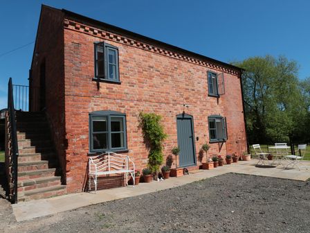 A brick building with gray windows and door with potted plants and outdoor furniture at Granary 1 Madley near Hereford