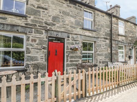 Stone cottage exterior with red door wooden fence metal chairs and bench at Preswylfa in Penmachno