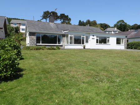A single story house with large windows and a grass lawn in front at Cae Glas in Pwllheli