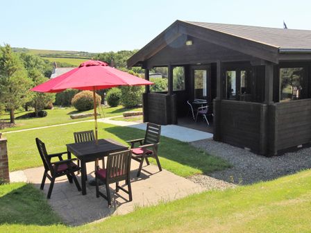 An outdoor patio area with a table, four chairs, and a red umbrella next to a wooden cabin at Hazel Lodge Lanivet near Bodmin