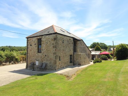 An outdoor view of a stone house with patio furniture and a garden with a red umbrella at Sunnywell Lanivet near Bodmin