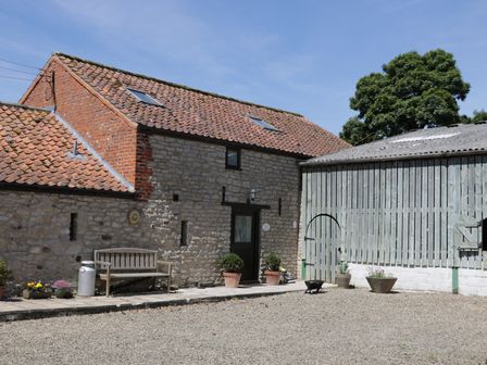 The exterior of a stone and brick building with a wooden bench and potted plants next to a wooden barn at The Old Hayloft in Kirkbymoorside
