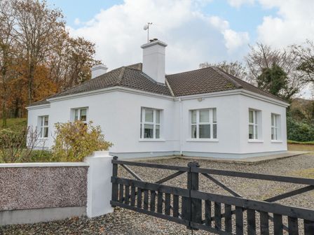 A white single-story house with a tiled roof behind a black wooden gate at DonRoss Cottage Pontoon County Mayo