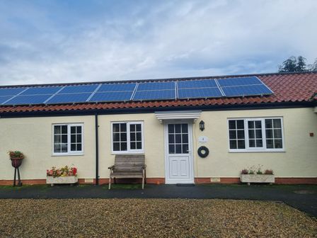 A cottage with solar panels on the roof a white door and windows flower pots and a wooden bench outside Richmond Cottage in Burythorpe near Malton