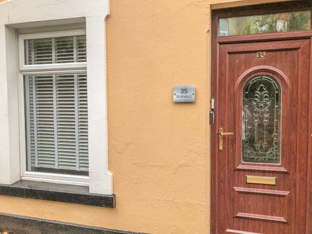A wooden door with decorative glass and a window with white blinds on a yellow wall at Sunvale in Teignmouth