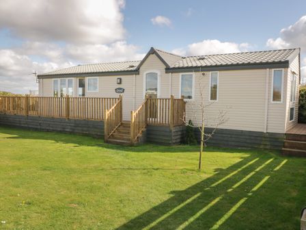 A mobile home with wooden steps and railing on a grass lawn at Coed Llai Lodge in Trearddur Bay