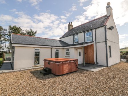 An exterior view of a two-story house with a hot tub on a gravel yard at Bryn Ffynnon in Bryncroes near Aberdaron
