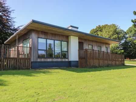 A wooden cabin with large windows and a fenced patio on a grassy lawn at Hazel in Truro