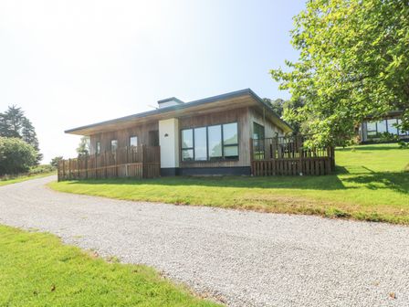 A single story house with wooden fencing around a gravel driveway and grass at Willow in Truro
