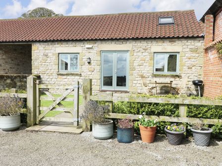 Front of a stone house with a wooden gate and fence with several potted plants on the ground at Stone Cross in Spaunton near Hutton-Le-Hole