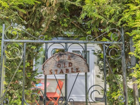 A metal gate with a wooden sign saying The Old Stable surrounded by greenery at The Old Stable in Far Forest