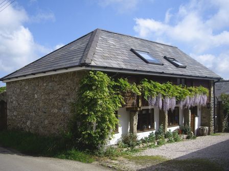 A stone and white wall house with a tiled roof and hanging purple flowers at The Linhay in Throwleigh