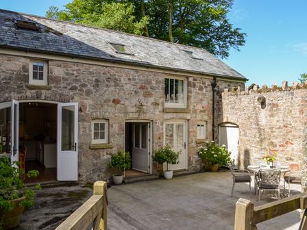 An outdoor stone patio with a round dining table and chairs outside a stone building at Butterbrook Coach House in Harford near Ivybridge