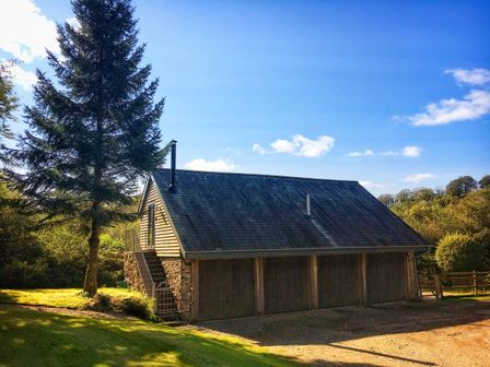 A building with wooden garage doors and an external staircase surrounded by trees and grass at The Linhay in Lydford