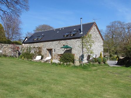 A stone house with a slate roof and skylights surrounded by grass and trees at Butterdon Barn in Moretonhampstead