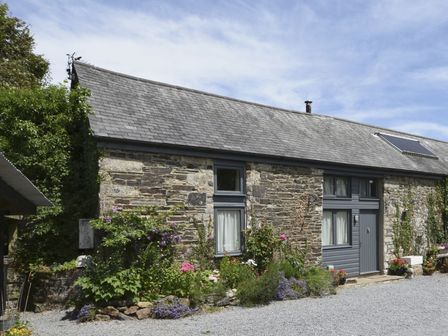 Stone cottage with slate roof windows and door surrounded by flowers and gravel at The Stone Barn Cottage in Holne