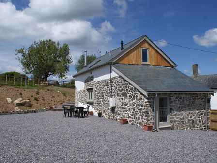 Stone and white exterior house with a gravel yard and plastic outdoor chairs at Bowbeer Barn in Drewsteignton