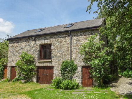 A stone building with wooden doors and a small balcony surrounded by greenery at Townend Barn in Lydford