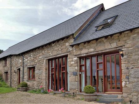 A stone house with wooden framed windows and doors with plants in pots outside at The Bolthole in Throwleigh near Chagford