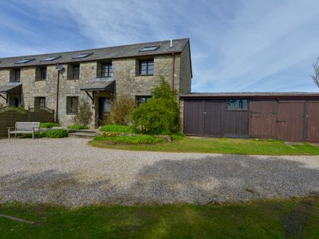 A stone cottage with multiple windows a bench a gravel driveway and wooden sheds at Ludgate Cottage in Haytor Vale
