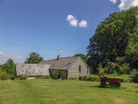 A stone and wood house with a grassy yard and trees under a blue sky at The Bakehouse in Gidleigh
