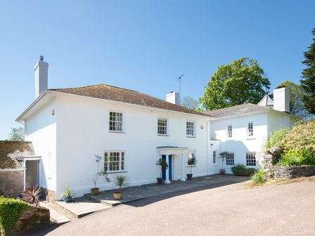 The exterior of a white two-story house with multiple windows and potted plants on a paved area at Sandridge Barton in Stoke Gabriel