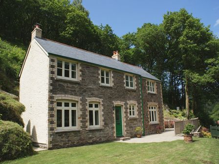 A stone cottage with multiple windows and a green door surrounded by trees and grass at Glenview in Barbrook near Lynmouth