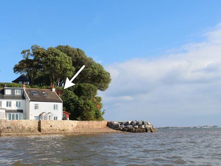 A house by the water with a stone wall and trees behind at 1 The Quay in Lympstone