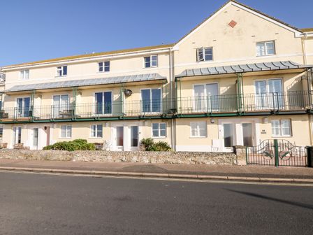 A row of yellow residential buildings with balconies and entrance doors along a street at 6 Lyme Mews in Seaton Devon