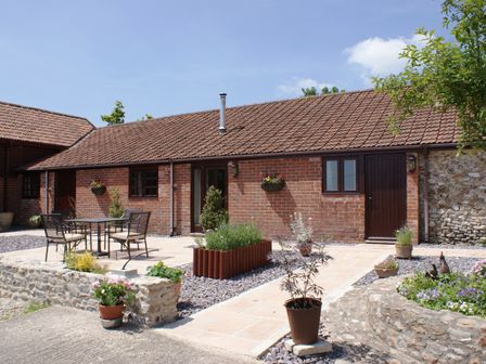 A brick building with a tiled roof and a patio with table and chairs at The Shippen in Colyton