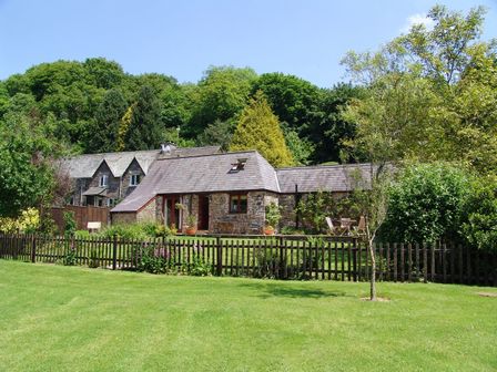 A stone house with a wooden fence in front and green trees at Honey House in Combebow near Bridestowe
