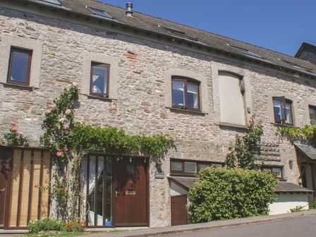 A stone cottage with multiple windows and doors with plants growing on the facade at Linney Cottage in Dittisham