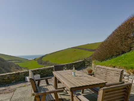 An outdoor patio with a wooden table and chairs overlooking green hills and the sea at Ayrmer House in Ringmore