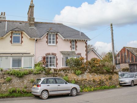 A stone wall with plants and two cars parked in front of a two-story house with brick trim near a wooden barn at The Old Post Office in Down Thomas near Plymouth