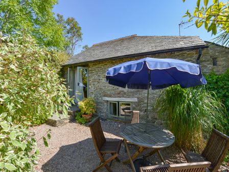 A garden patio with wooden table and chairs under a blue umbrella outside a stone building at Parsonage Farm Cottage in Newton Ferrers
