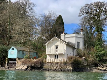 A cream house and a blue cabin on the water's edge surrounded by trees at The Bathing House in Ashprington