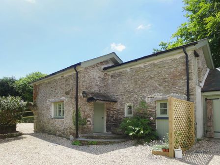 An exterior stone building with multiple windows and doors surrounded by gravel and plants at Torrings Barn in Aveton Gifford