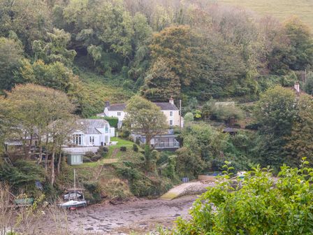 Houses surrounded by trees on a hillside near a small boat dock and riverbank at Junket Cottage in Noss Mayo