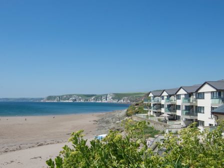 A beach with sand and people near the sea with a row of buildings on the right and cliffs in the background at 24 Burgh Island Causeway in Bigbury-on-Sea