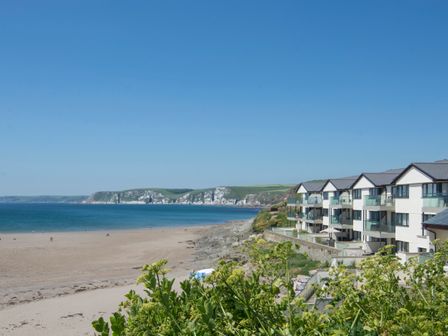 A sandy beach with rocks and water near apartment buildings at 23 Burgh Island Causeway in Bigbury-on-Sea