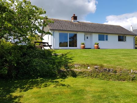 A single story white house with a tiled roof and a grassy garden with a picnic table at Orchard View in Kellaton near Hallsands