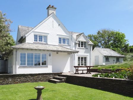 A white two-story house with multiple windows a stone patio a wooden table a stone wall and a green lawn at Ayrmer Path in Ringmore